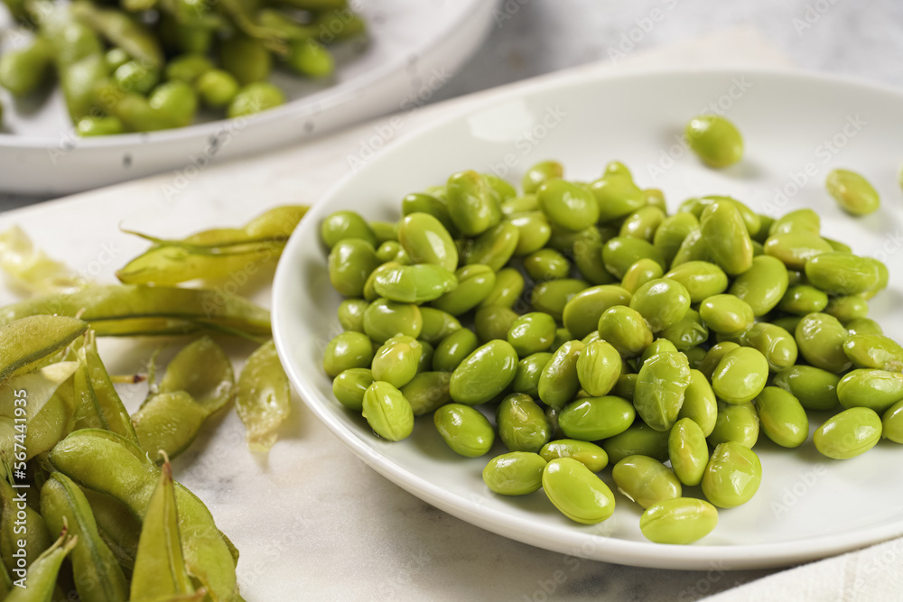 Peeling fresh steamed green soy beans edamame. Japanese plant snack on marble board on light grey background Peeling fresh steamed green soy beans edamame. Japanese plant snack on marble board on light grey background