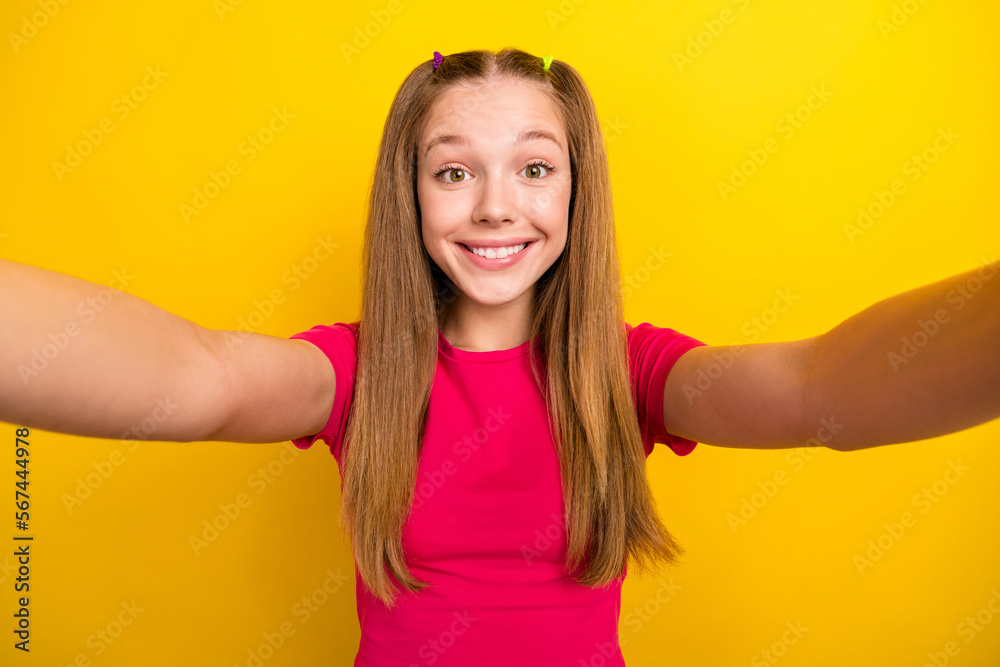Photo of satisfied adorable schoolgirl with straight hairstyle wear pink t-shirt making selfie isolated on yellow color background Photo of satisfied adorable schoolgirl with straight hairstyle wear pink t-shirt making selfie isolated on yellow color background