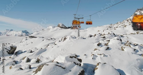Orange chair lift ride at Samnaun Ischgl ski resort, above rocky terrain covered with snow on the border of Austria and Switzerland. Winter, skiing, chairlift.
