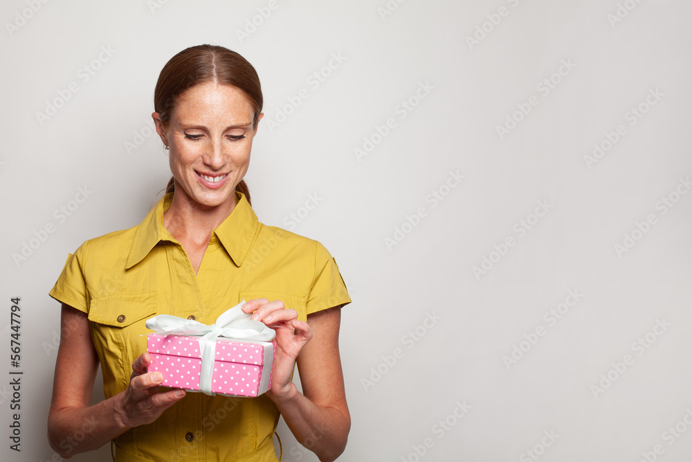 Cute smiling woman opening pink gift present box on grey background