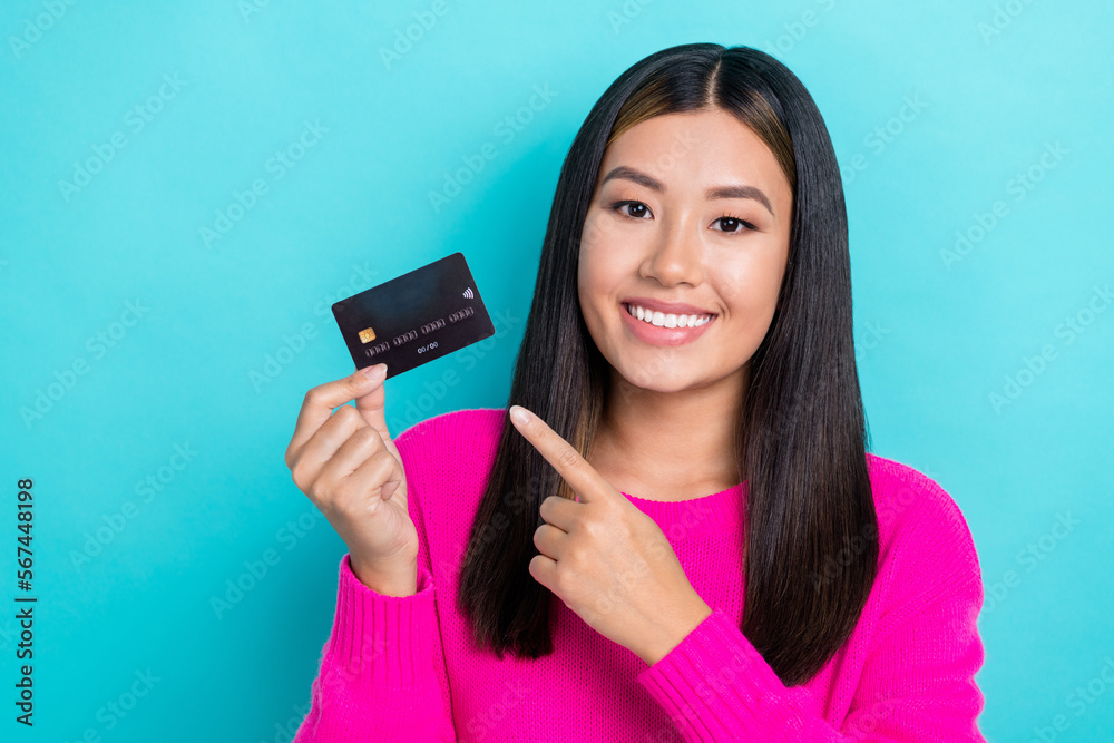Portrait photo of young gorgeous charming korean business lady wear pink pullover direct finger new black bank card isolated on cyan color background Portrait photo of young gorgeous charming korean business lady wear pink pullover direct finger new black bank card isolated on cyan color background