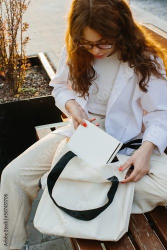 Magazine or book image mockup. A young hipster girl at a table in a coffee shop takes out a magazine from a canvas shopper bag. photo