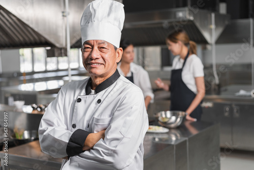 Confident Asia senior chef with assistant woman chef and kitchen background