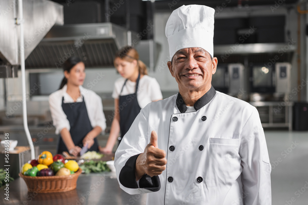 Thump up Asia senior chef with assistant woman chef and kitchen background