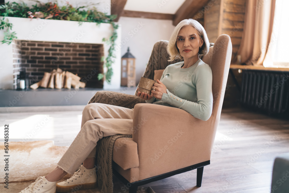 Senior woman with cup of coffee sitting on armchair in living room