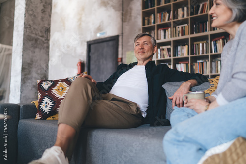 фотографія Cheerful senior man sitting on couch with crop woman having drink