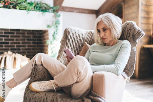 Mature woman browsing smartphone while sitting on sofa