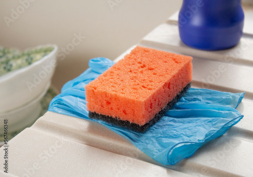 Close-up orange sponge for washing dishes and gloves on the edge of kitchen sink