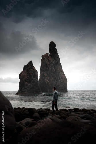 a man standing before Miradouro da Ribera da Janela,The sea stacks located just a few meters from the coast, The waves crashing on the rock formations, The volcanic cliffs and its basalt structures,
