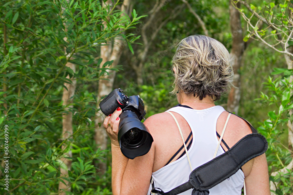 Woman tourist walking on a trail in the middle of the woods carrying a camera Woman tourist walking on a trail in the middle of the woods carrying a camera