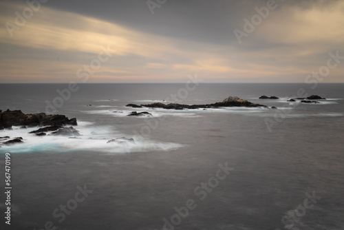 Sunset at Point Lobos State Natural Reserve, long exposure, featuring the ocean and rocks against a partly cloudy sky with orange hues. Carmel, California, USA.