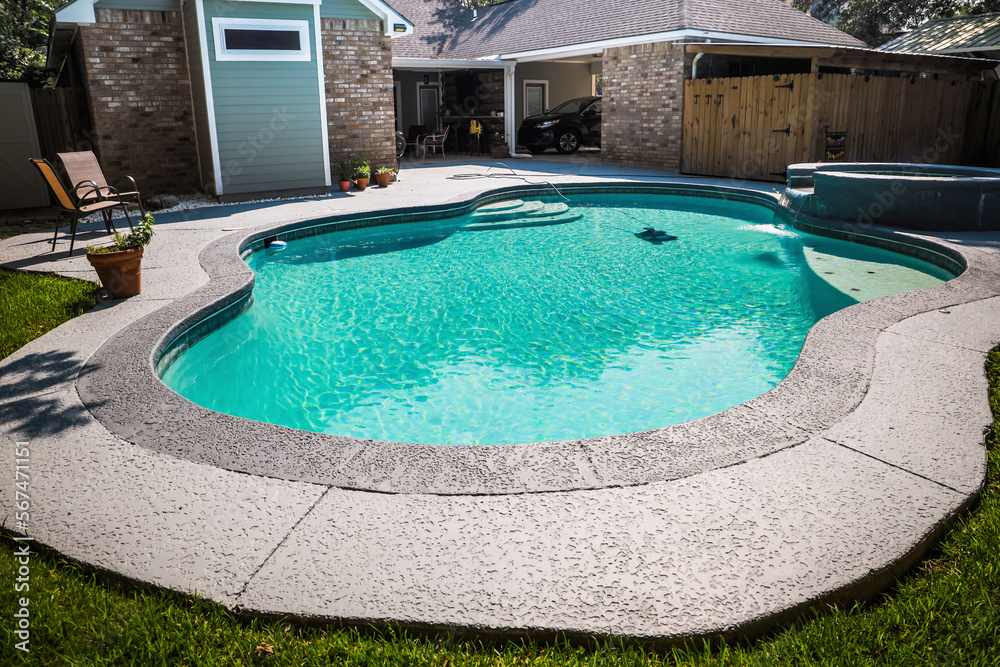 A large free form gray grey accent swimming pool with turquoise blue water in a fenced in backyard