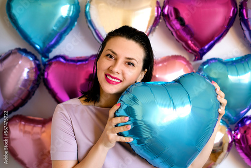 A beautiful young woman with bright pink lips holds a heart-shaped balloon in her hands on Valentine's Day