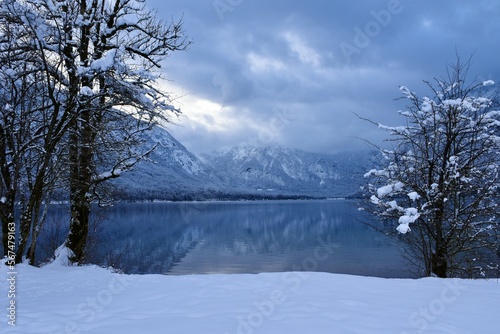 View of Bohinj lake in Gorenjska, Slovenia in winter with forest covered mountain slopes of Julian alps rising above