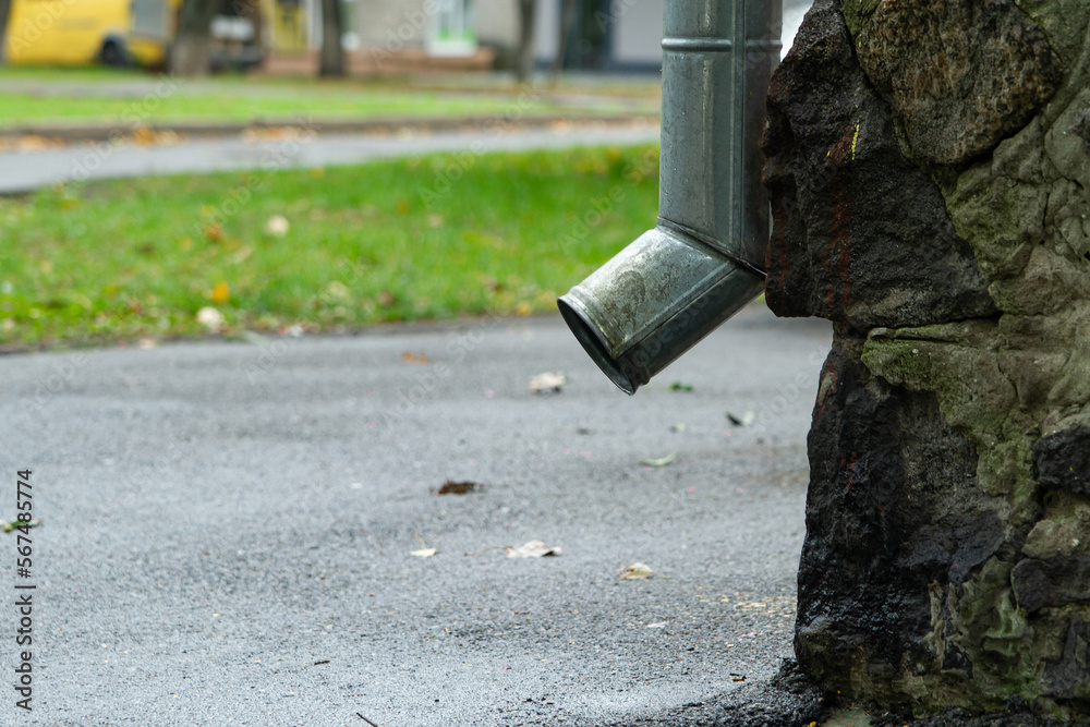 Downspout of rain gutter near the side of a house, side view. Bottom of