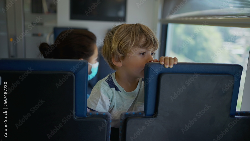 Child passenger travels by train standing on seat. Authentic real life male kid traveling on transportation Child passenger travels by train standing on seat. Authentic real life male kid traveling on transportation