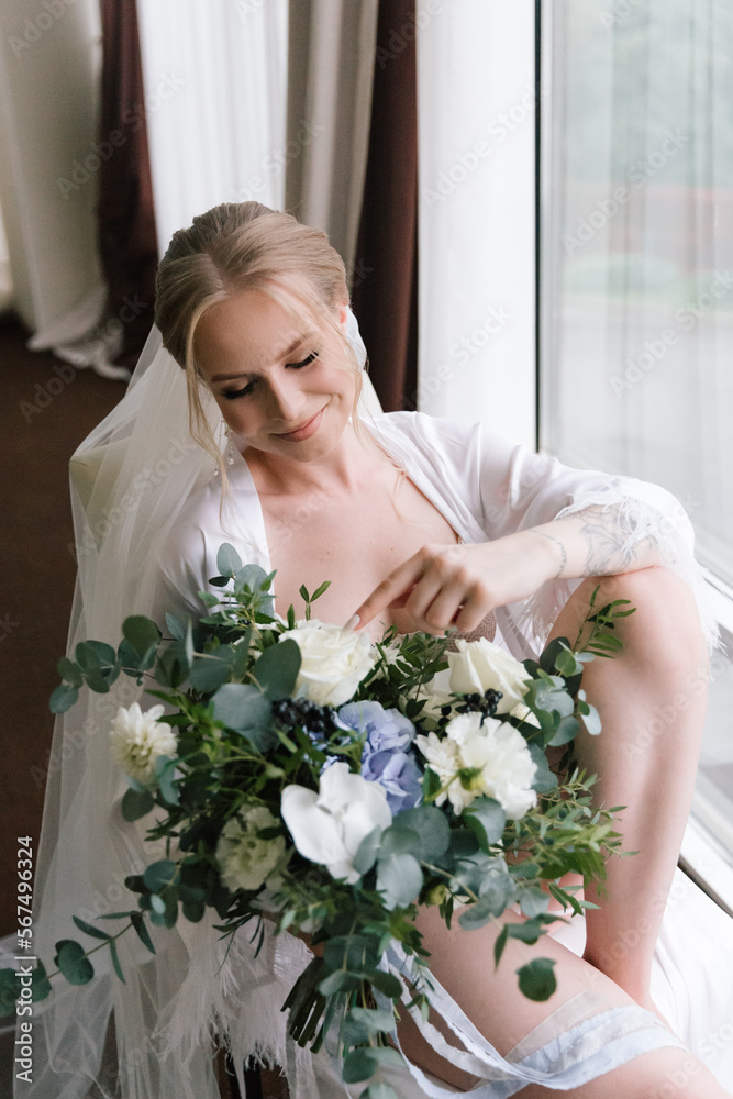 Morning preparations of a beautiful, sexy bride with a wedding bouquet in lingerie, a bathrobe in a hotel, where she puts on shoes in a wedding dress Morning preparations of a beautiful, sexy bride with a wedding bouquet in lingerie, a bathrobe in a hotel, where she puts on shoes in a wedding dress