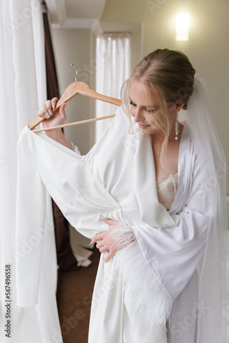 Morning preparations of a beautiful, sexy bride with a wedding bouquet in lingerie, a bathrobe in a hotel, where she puts on shoes in a wedding dress