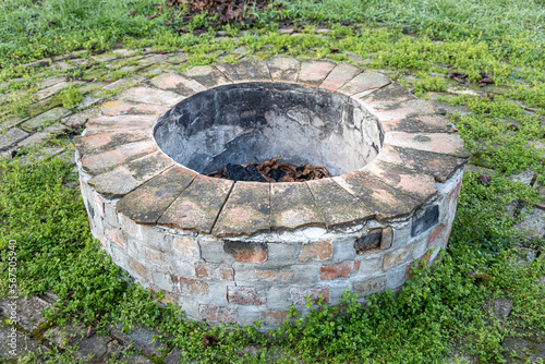 Gray and brown round fire hearth with orange bricks for a bonfire on green grass in a summer forest