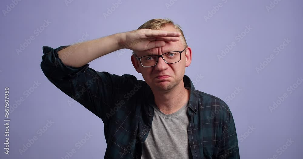 Caucasian man in eyewear looking far away with hand over head, studio shot Caucasian man in eyewear looking far away with hand over head, studio shot