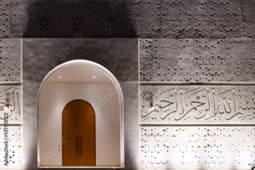 Illuminated entrance doors and facade of white Mosque of Light in Dubai, with Quran verses and triangular geometric patterns. photo