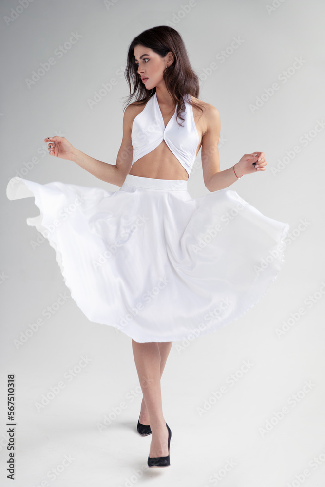 Naklejka premium Full length image of young woman with hairstyle and makeup in white dress posing in studio, it spins, isolated grey background.