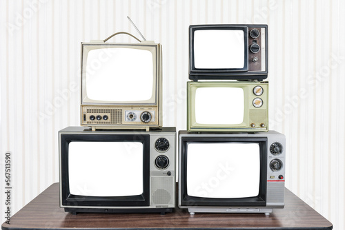 Five vintage televisions on old wood table with wall paper background and empty cut out screens. 