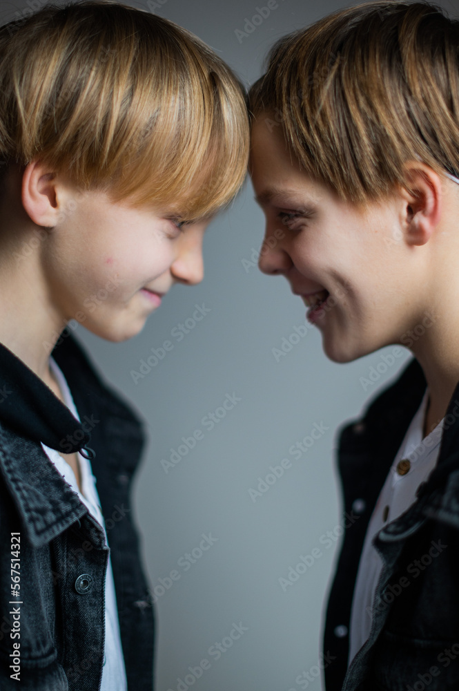 Two happy boys, happy brothers who are smiling happily together. Brothers stay on grey background. modern tenagers.book cover Two happy boys, happy brothers who are smiling happily together. Brothers stay on grey background. modern tenagers.book cover
