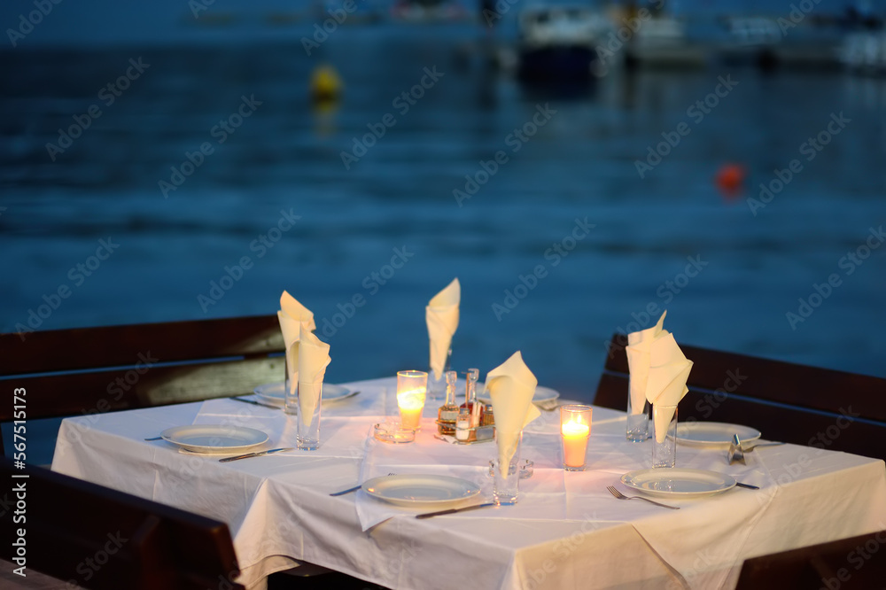 An empty open European cafe on the seashore at dusk. Stylish table decoration with a burning candle. An vacant table.