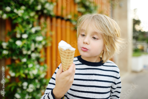 Happy little boy eating tasty ice cream cone outdoors during family stroll. Child have a snack on the go. Gelato is loved delicacy of kids. Sweets are unhealthy food for baby. Diabetes risk
