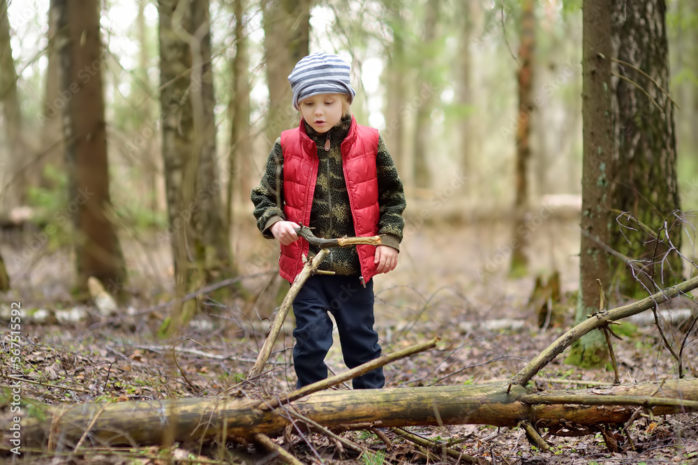 Little boy in red vest is playing with big branch and having fun in forest on early spring day. Activity for children. Outdoor recreation for family Little boy in red vest is playing with big branch and having fun in forest on early spring day. Activity for children. Outdoor recreation for family