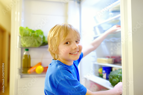 Cute preteen boy independently taking products from refrigerator at home. Child choosing between healthy and unhealthy food. Intuitive nutrition, conscious nutrition