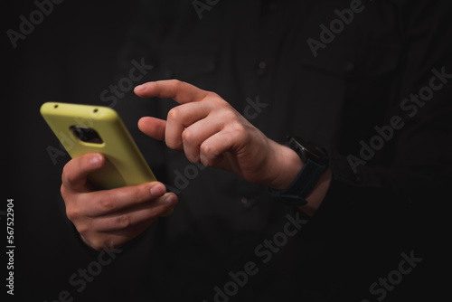 man dressed in black, checks his smart phone with a gesture in his hand to perform an action, black background
