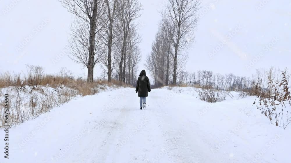 Woman walking on snowy road in overcoat in winter. Snow and blizzard on countryside road. Woman walking on snowy road in overcoat in winter. Snow and blizzard on countryside road.