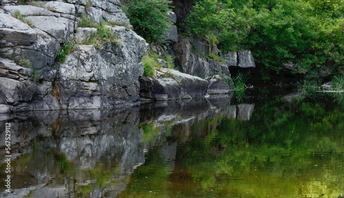 Widescreen landscape of huge steep rocks, river and lush greenery in ancient granite canyon Buky in Ukraine in summer, view from water with colorful reflections, scenic touristic attraction
