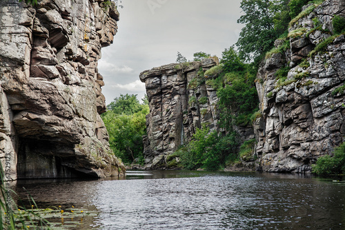 Landscape of huge majestic rocky cliffs, shores and lush greenery in ancient granite canyon Buky in Ukraine, view from water of mountain river in summer, popular place for tourism and climbing photo