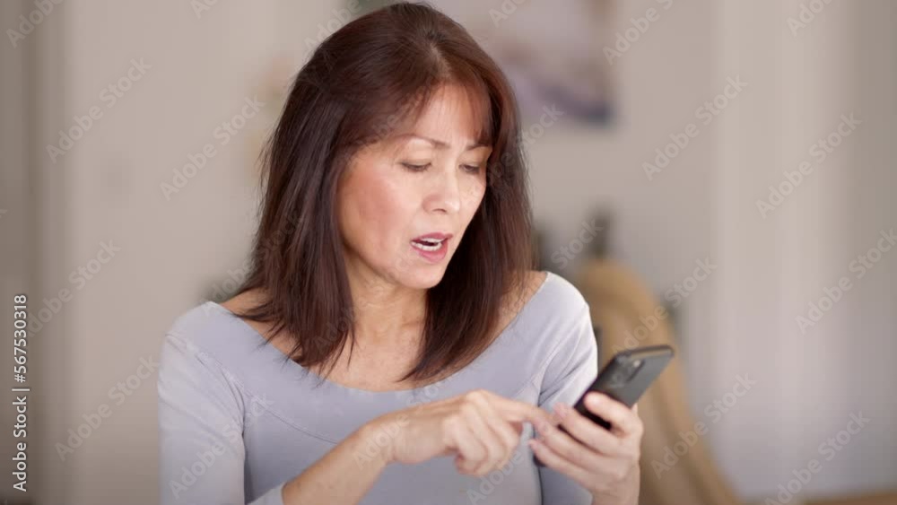 Smiling attractive mature woman in blue top relaxing scrolling mobile phone sitting in leisure home living room Smiling attractive mature woman in blue top relaxing scrolling mobile phone sitting in leisure home living room