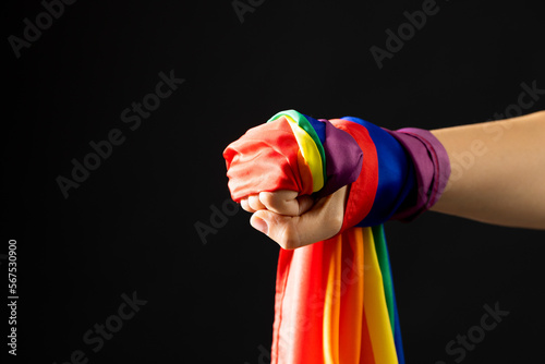 Hand holding rainbow coloured flag with copy space on black background
