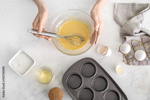 Woman preparing delicious muffins on light background