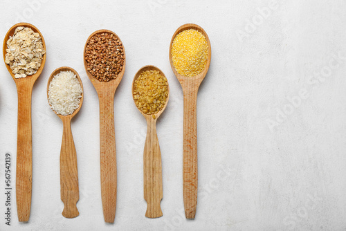 Wooden spoons of different cereals on light background