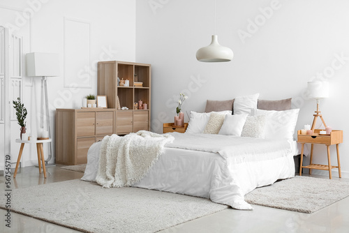 Interior of bedroom with bed  shelving unit  burning candles and houseplants near white wall