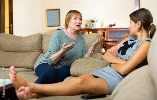 Angry senior woman and depressed daughter sitting at sofa, quarrel at home interior
