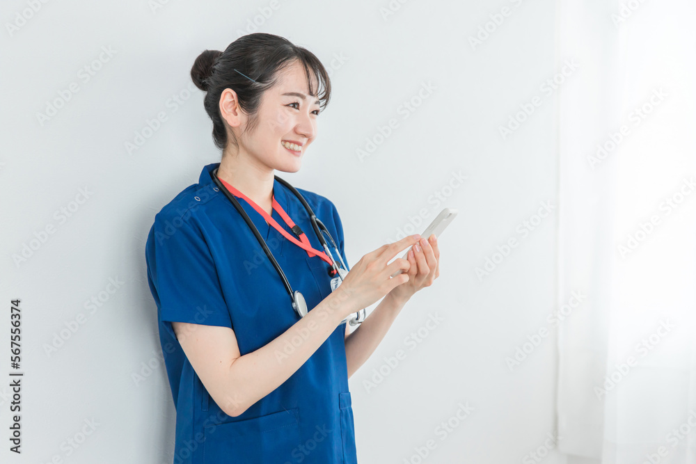 スマホを持った青いクリニックユニフォームの医療従事者の女性(医者・医師)
スマホを持った青いクリニックユニフォームの医療従事者の女性(医者・医師)