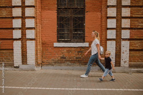 Mom and son walk in the summer in the city along the brick wall of the building