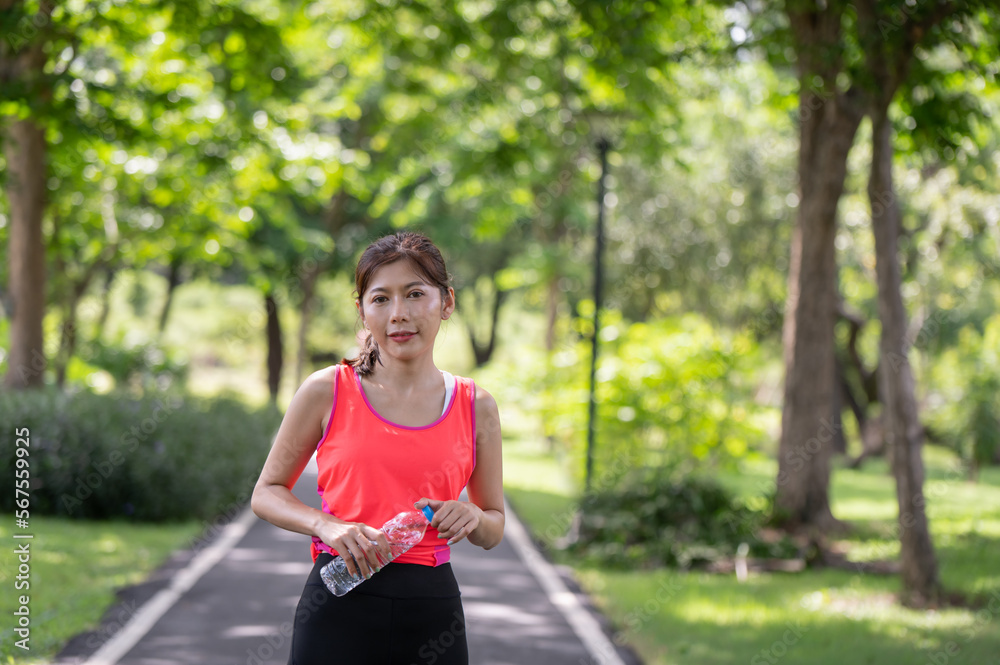 Asian female runner standing outdoors holding water bottle in the park Asian female runner standing outdoors holding water bottle in the park