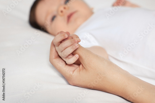 Mother holding hand of her little baby on bed, closeup
