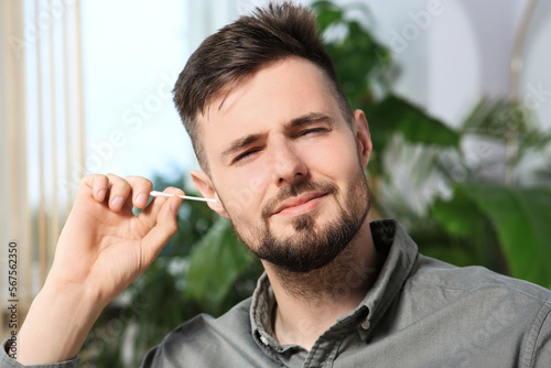 Young man cleaning ear with cotton swab at home