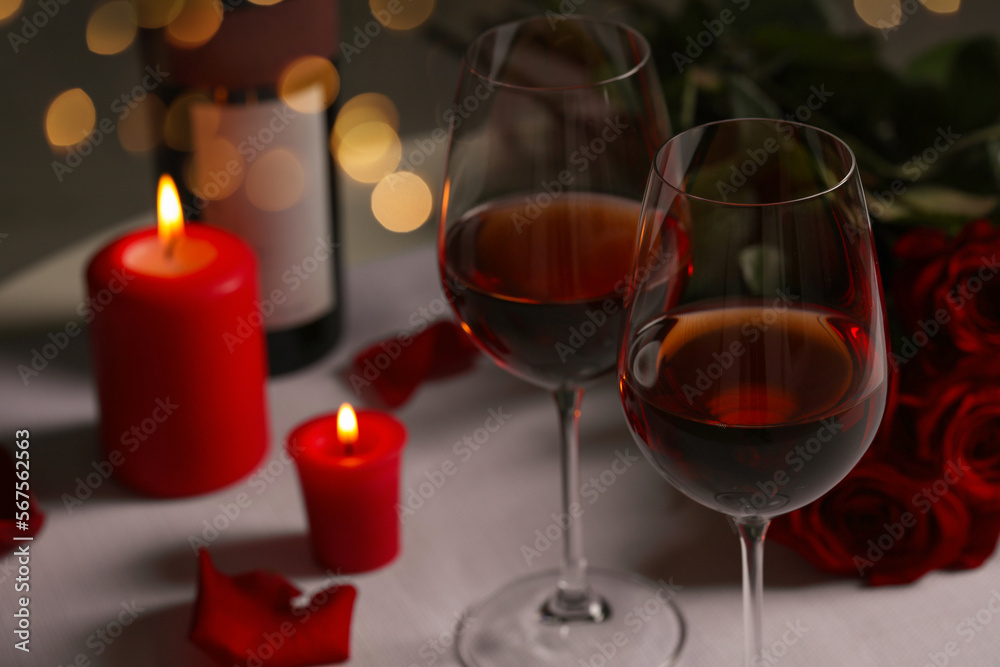 Romantic table setting with glasses of red wine, rose flowers and burning candles Romantic table setting with glasses of red wine, rose flowers and burning candles