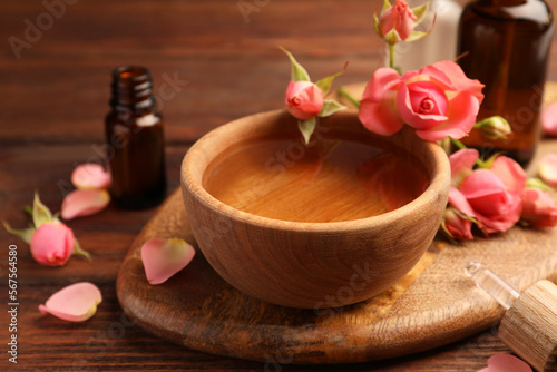 Bowl of essential oil and beautiful roses on wooden table. Aromatherapy treatment