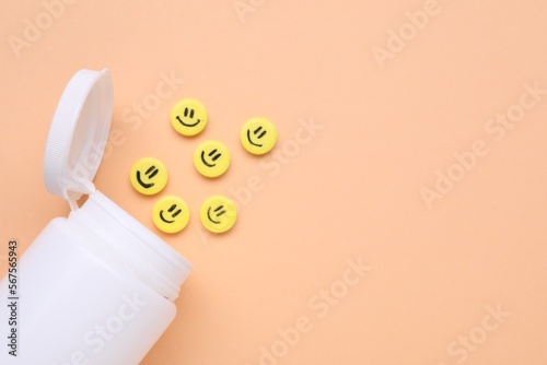 Bottle and yellow antidepressant pills with happy faces on pale orange background, flat lay. Space for text